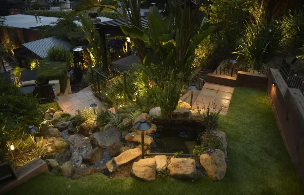 Well-lit garden pathway and pond, an example of properly maintained landscape lighting